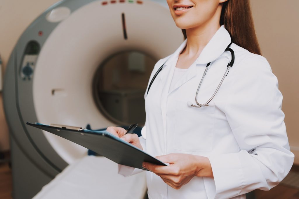 Close up of a female doctor holding a clipboard in front of an MRI machine